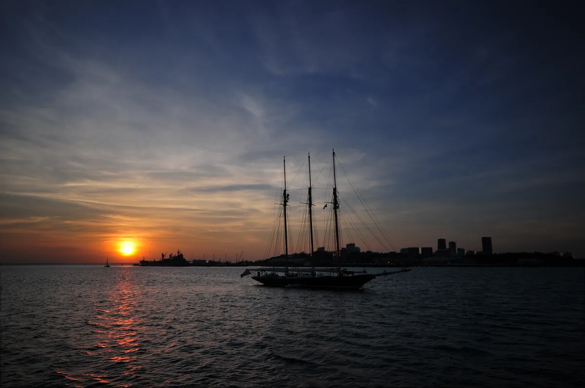 Sunset over Darwin Harbour with a sailing ship and the city skyline
